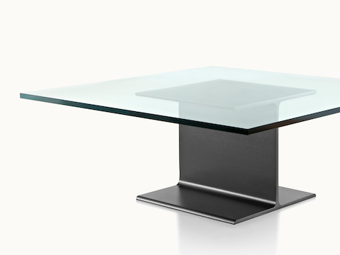 Partial angled view of a square I Beam coffee table with a glass top and black cast-aluminum pedestal.