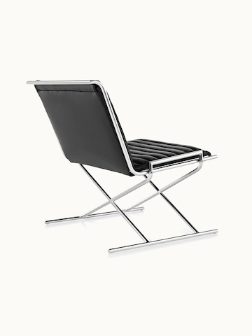 A Sled lounge chair with ribbed black leather upholstery and an X-shaped steel frame, viewed from behind at an angle.