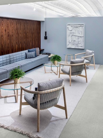 A lounge featuring a light blue Tuxedo Classic Lounge Seating sofa, three light gray Crosshatch Chairs, and three round Loophole occasional tables.
